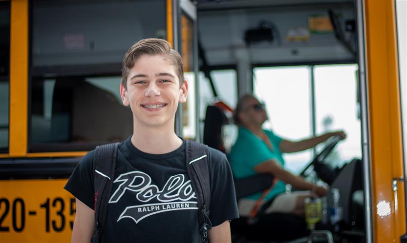 A student smiles outside of a school bus